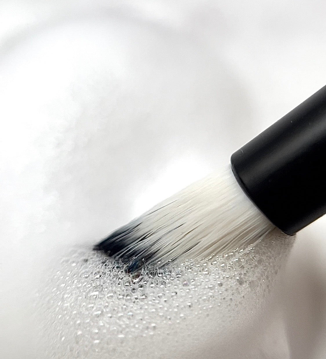 Oil-free lash shampoo being lathered with a lash cleansing brush, demonstrating how to clean eyelash extensions in hot weather.