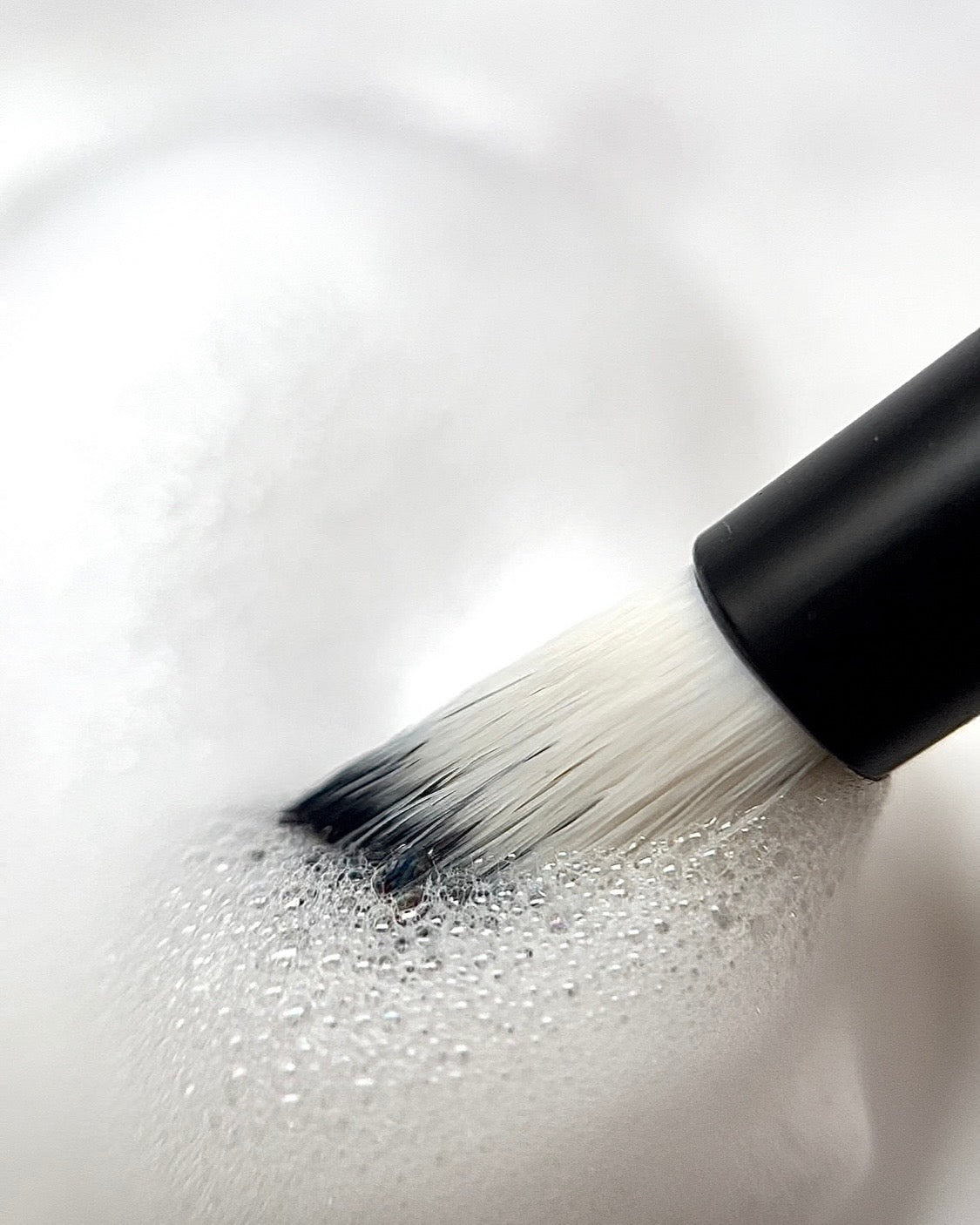 Oil-free lash shampoo being lathered with a lash cleansing brush, demonstrating how to clean eyelash extensions in hot weather.